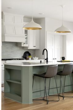 a kitchen with white cabinets and green island in the center, two pendant lights hanging from the ceiling