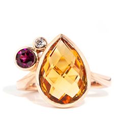 Beautifully crafted in 9 carat gold, The Angie Ring is a stunningly eccentric design. Her golden tear shaped citrine. her purple garnet and her shimmering diamond are wrapped in satiny gold celebrating a love of colour and a rich imagination.  The Angie Ring Gem Details The pear shape checkerboard cut citrine is a bright orange colour and measures approximately 14.8x10.4 millimetres. The bright purplish red round garnet measures approximately 4.4 millimetres. The round brilliant cut diamond is e Orange Gemstones, Purple Garnet, Garnet And Diamond Ring, Orange Colour, Contemporary Ring, Pear Cut, Vintage Jewellery, Round Brilliant Cut Diamond, Pear Shape