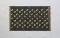 a black rug with brown and yellow flowers on it hanging from a wall in front of a white wall