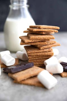 a stack of crackers with marshmallows and chocolate on the side next to a bottle of milk