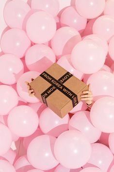 a person holding a box surrounded by pink balloons