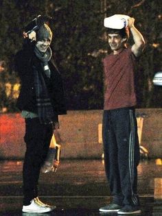 two young men standing next to each other in the rain at night, one holding up a white frisbee