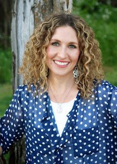 a woman with curly hair wearing a blue polka dot shirt and smiling at the camera