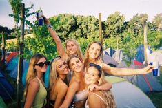 a group of young women standing next to each other in front of tents and trees