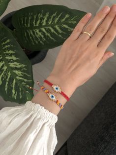 a woman's hand with two bracelets on it and a plant in the background