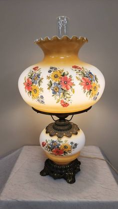 a vase with flowers painted on it sitting on a white table top next to a lamp