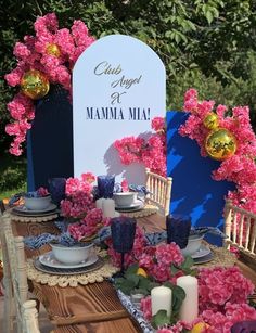 the table is set with pink flowers and blue chinaware for an outdoor tea party