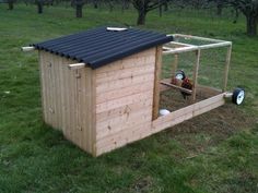 a chicken coop in the middle of a grassy field with trees and grass behind it