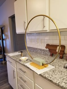 a kitchen with white cabinets and marble countertops has a circular mirror on the wall