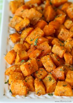 a white plate topped with cubed sweet potatoes covered in parmesan cheese and herbs