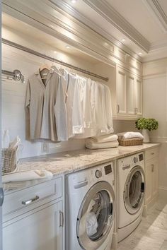 a washer and dryer in a white laundry room with clothes hanging on the rack