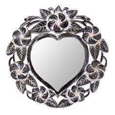 a heart shaped mirror sitting on top of a white wall with leaves and flowers around it