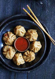 some dumplings with dipping sauce in a bowl next to chopsticks on a table