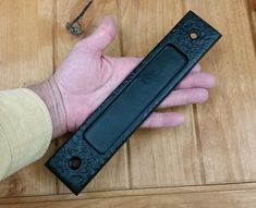 a hand holding a black leather case on top of a wooden table next to a bottle opener