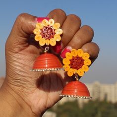 a hand holding two orange and yellow earrings with flowers on it's ear ends