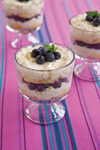 three desserts with blueberries and whipped cream in small glass dishes on a table