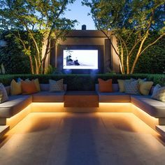 an outdoor seating area is lit up at night with lights on the benches and trees in the background