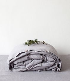 an unmade bed with grey sheets and green leaves on the top, in front of a white wall