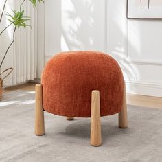 an orange footstool sitting on top of a carpeted floor next to a potted plant