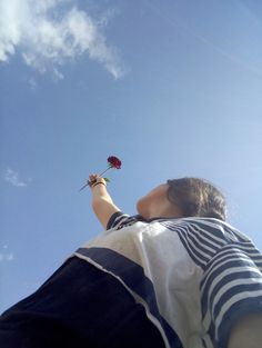 a woman is flying a kite with a rose in it's hand and looking up into the sky