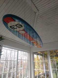 a surfboard hanging from the ceiling in a room with windows and potted plants