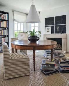 a dining room table surrounded by chairs and books in front of a fire place with a potted plant on top