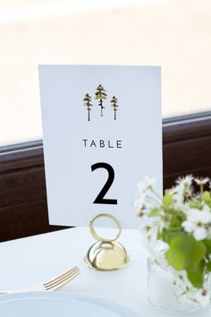 the table numbers are placed next to a vase with white flowers and greenery in it