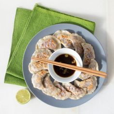 a plate topped with dumplings and dipping sauce next to chopsticks on a green napkin