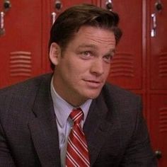 a man wearing a suit and tie sitting in front of lockers with red doors