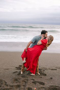 a man and woman are kissing on the beach with footprints in the sand behind them