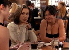 two women sitting at a table talking to each other in a restaurant with people eating and drinking