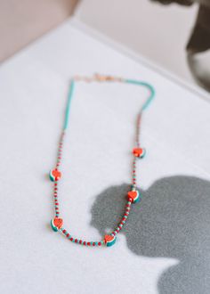 a necklace with red beads on it sitting on top of a white table next to a vase