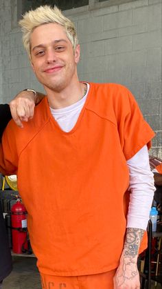 a man in an orange prison uniform pointing at the camera while another man stands next to him