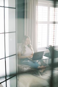 a woman sitting on a couch with a laptop in front of her and a cat looking out the window