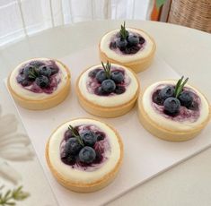 four blueberry cheesecakes are arranged on a white platter with rosemary sprigs