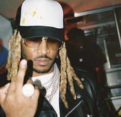 a man with dreadlocks and a hat pointing to the side while wearing a black leather jacket