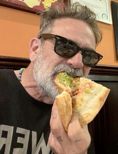 a man eating a sandwich in front of his face while wearing sunglasses and a black t - shirt