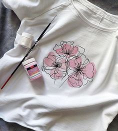 a white t - shirt with pink flowers on it next to some watercolor paints