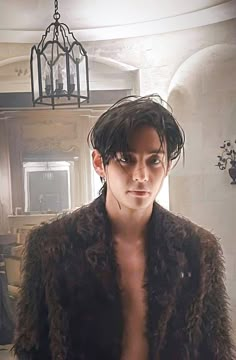 a shirtless man in a fur coat standing next to a chandelier hanging from the ceiling