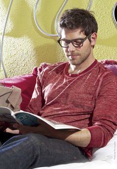 a man reading a book while sitting on a bed in front of a yellow wall