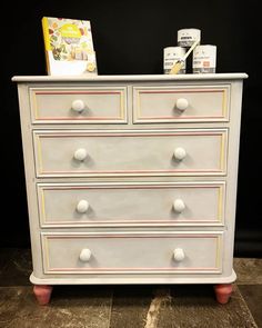 a white dresser with pink handles and knobs on the bottom drawer, next to a book