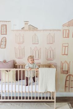 a baby in a crib next to a wall with houses drawn on the walls