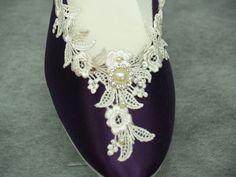 a pair of purple shoes with white lace and pearls on the heel, sitting on a gray surface