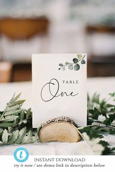 a place card sitting on top of a table with greenery and leaves around it