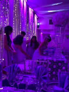 a group of people standing around a table with purple lights on the wall behind them