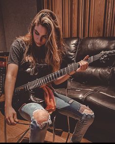 a woman sitting on a chair playing an electric guitar