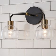 two clear glass globe lights hang on the wall above a white tile backsplash