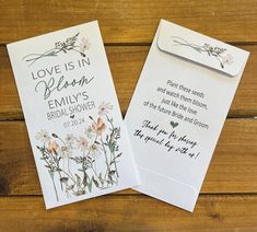 two wedding cards with flowers on them sitting on top of a wooden table next to each other