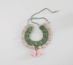 a green and white crocheted necklace with pink tassels on it's sides