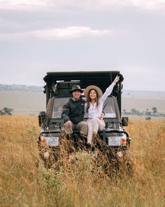 a man and woman sitting in the back of a truck on top of a grass covered field